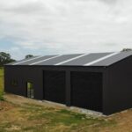 Black Australian-made steel shed in a grassy field with sliding windows, roller doors, and a skillion roof.