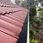 Gutter with installed brush guards on a red tile roof surrounded by a garden.