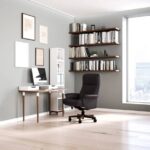 Modern home office with an ergonomic leather recliner chair, bookshelf, and a desk near a large window.