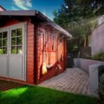 Red wooden storage shed with tools hanging on the side and a clean backyard, showcasing a neat and organized outdoor space.